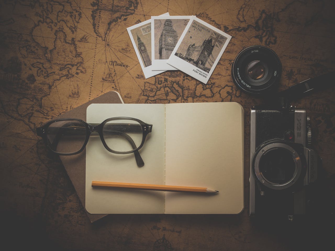 gallery-5 Flat lay of travel essentials including camera, notebook, eyeglasses, and map for adventure planning.
