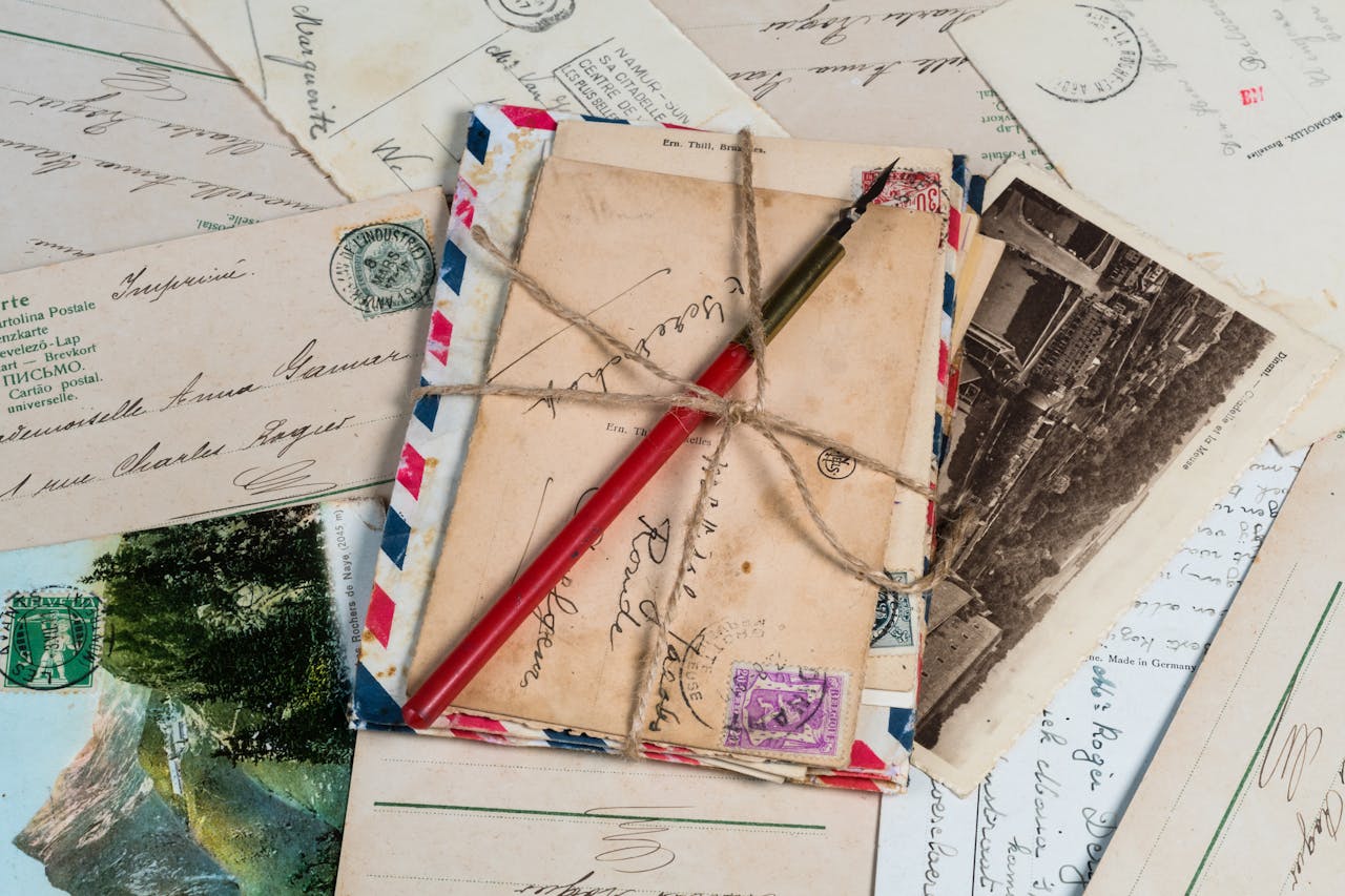 hero-img-01 A collection of vintage postcards and envelopes tied with twine, featuring a pen and old stamps.