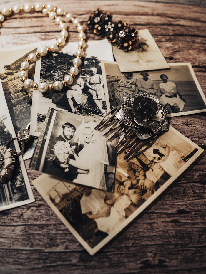 A collection of vintage black and white photos with pearl necklace and antique brooch displayed on a rustic wooden table.